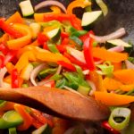 colorful vegetables in a pan with a wooden spoon stirring