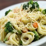 Plate of cooked tortellini and Alfredo sauce with broccoli and carrots garnished with shredded Parmesan cheese