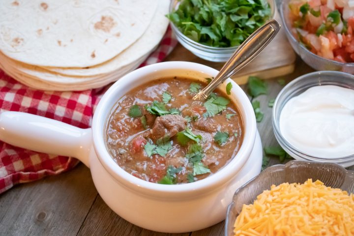 Serve carne guisada with tortillas, sour cream, pico de gallo, shredded cheese, and cilantro