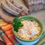Homemade Pimento Cheese in a green and white bowl, garnished with a sprig of parsley. There is an unpackaged loaf of sliced bread at the top of the photo.