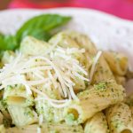 Rigatoni on a white plate topped with shredded parmesan cheese and pesto.