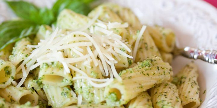Rigatoni on a white plate topped with shredded parmesan cheese and pesto.