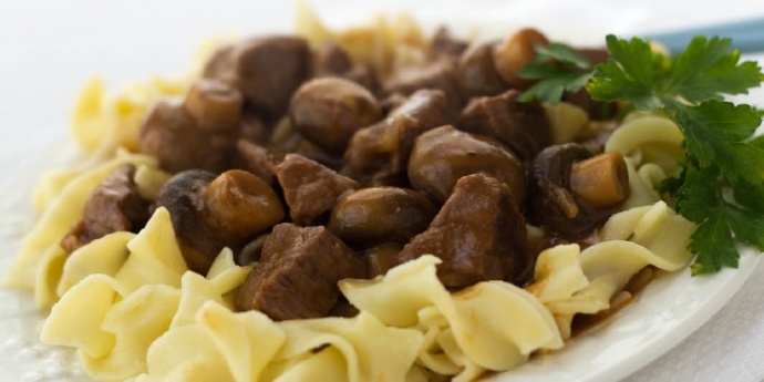 Slow Cooker Beef with Mushrooms White plate with egg noodles topped with beef and mushrooms, garnished with a sprig of parsley.