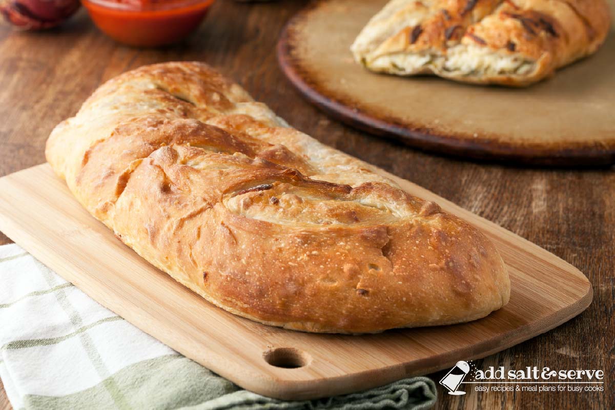 Vegetable Stromboli on a cutting board with a slice of stromboli in the background.