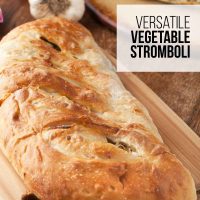 Vegetable Stromboli on a cutting board with a slice of stromboli in the background surrounded by a garlic bulb and a dish of marinara sauce.