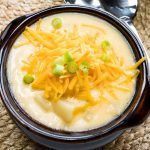 Potato soup in a brown soup bowl, topped with shredded cheddar cheese and garnished with chopped green onions.