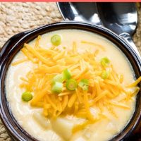 Potato soup in a brown soup bowl, topped with shredded cheddar cheese and garnished with chopped green onions. Two spoons are on the brown placemat beside the bowl. Text 30 minute Hash Brown Soup add salt & serve formerly menus4moms