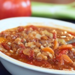 Soup with barley, lentils, carrots, tomatoes, and broth in a white bowl