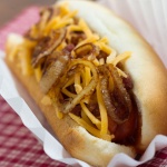 hot dog in bun topped with sauteed onion and grated cheddar cheese.