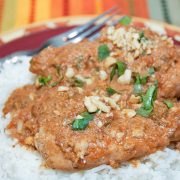 Chicken breasts cooked with peanut sauce over white rice and garnished with chopped cilantro and peanuts