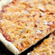 Slice of pizza topped with chicken, cheddar cheese, and barbecue sauce being lifted from the pie.