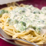 Afredo sauce with broccoli over fettuccine on a clear glass plate with a fork