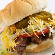 White bun piled with grilled flap meat, lettuce, tomato, cheese, and jalapeno slices