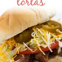White bun piled with grilled flap meat, lettuce, tomato, cheese, and jalapeno slices. Text is Carne Asada Tortas - Add Salt & Serve logo