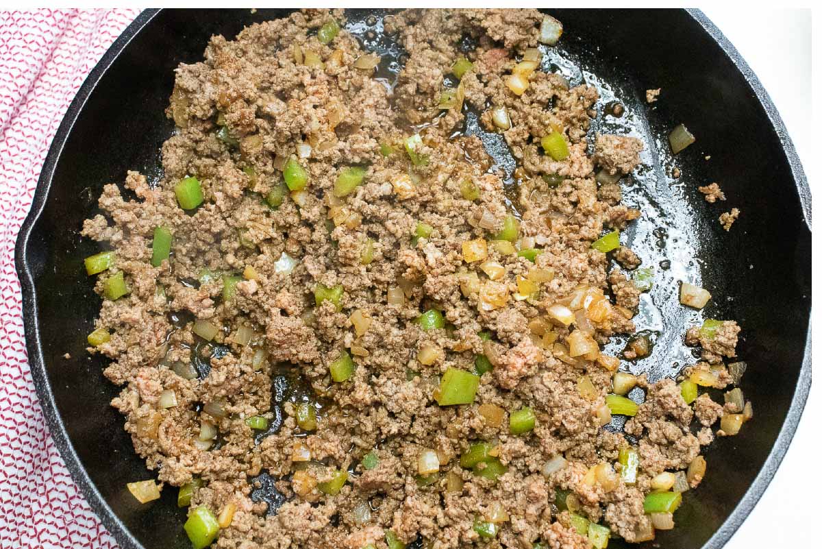 Cooked ground beef, diced onions and bell peppers in a cast iron skillet.