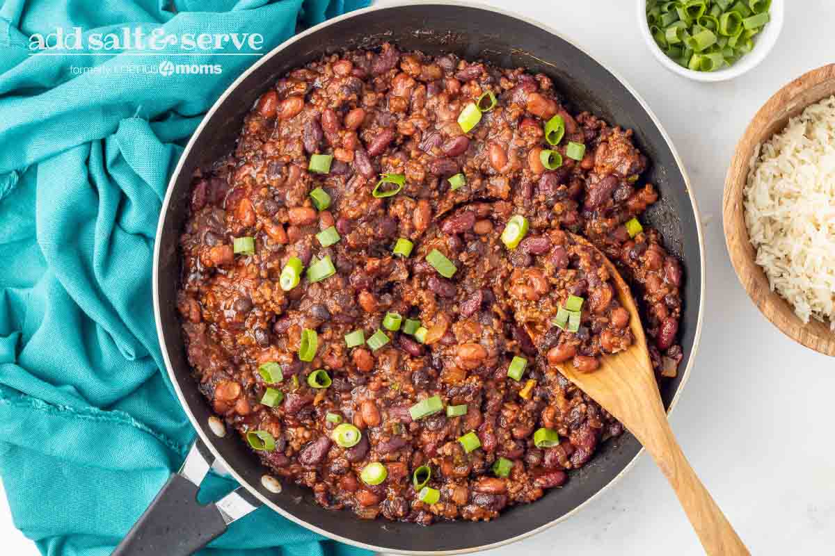 Beef and beans garnished with green onion in a skillet with a wooden spoon.