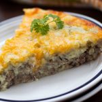 White plate with slice of cheeseburger pie and sprig of parsley