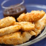 Breaded chicken strips on a glass plate with barbecue sauce in a condiment cup