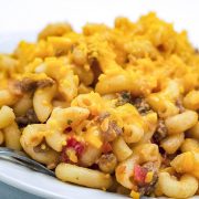 White bowl of macaroni noodles, ground beef, and tomatoes topped with shredded cheddar cheese