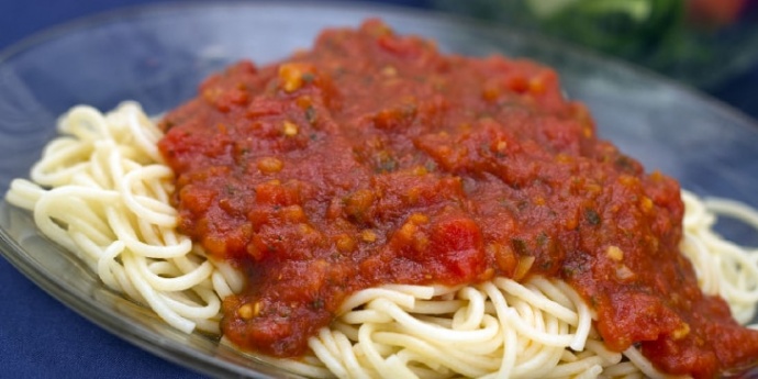 A pile of cooked spaghetti noodles covered with marinara sauce on a blue plate