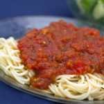 A pile of cooked spaghetti noodles covered with marinara sauce on a blue plate