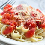 White plate with fettuccine and tomato sauce, topped with Parmesan cheese