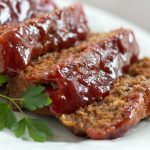 Slices of glazed meatloaf on a white plate.