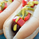 Bratwurst on a hotdog bun with mustard, diced red and green bell peppers and diced onions