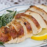 slices of roasted chicken garnished with fresh rosemary and lemon slices on a white plate