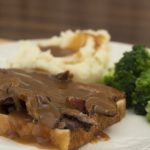 Photo of a slice of white bread with sliced roast beef and gravy, with mashed potatoes and gravy and cooked brocoli florets on a white plate