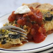 Photo of a fork cutting into a slice quiche topped with salsa and sour cream