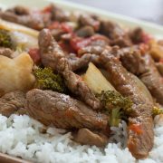 Cooked strips of beef with onions, brocolli florets, diced tomatoes, and mushrooms on a bed of rice
