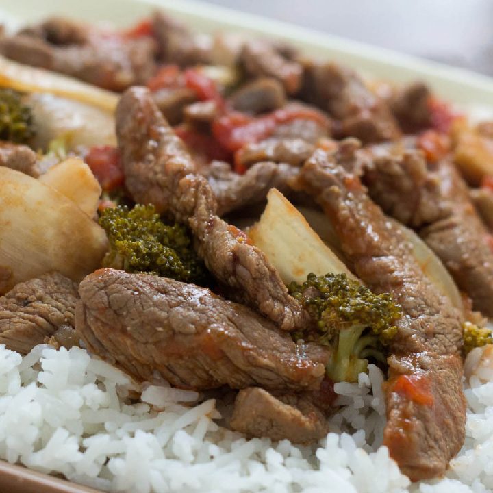 Cooked strips of beef with onions, brocolli florets, diced tomatoes, and mushrooms on a bed of rice