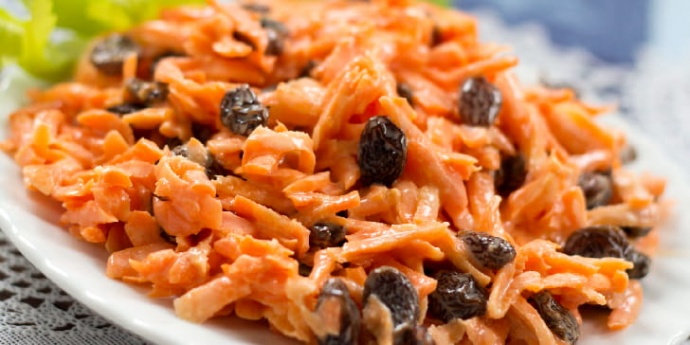 Carrot Raisin salad on a white plate garnished with celery leaves
