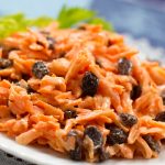 Carrot Raisin salad on a white plate garnished with celery leaves