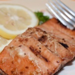 Pieces of cooked salmon on a white plate with a fork, garnished with two lemon slices and parsley