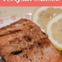 Pieces of cooked salmon on a white plate with a fork, garnished with two lemon slices. Text Easy Baked Teriyaki Salmon Add Salt & Serve formerly Menus4Moms