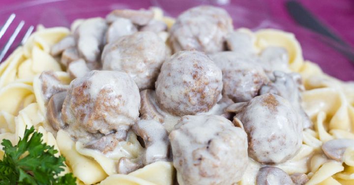 Wide egg noodles and meatballs topped with a mushroom sauce on a purple plate, garnished with parsley
