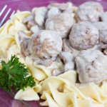 Wide egg noodles and meatballs topped with a mushroom sauce on a purple plate with a fork, garnished with parsley