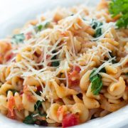 Spiral pasta mixed with diced tomatoes and spinach, topped with shredded parmesan cheese