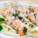 White plate with shrimp, minced garlic, and parsley on a bed of fettuccine