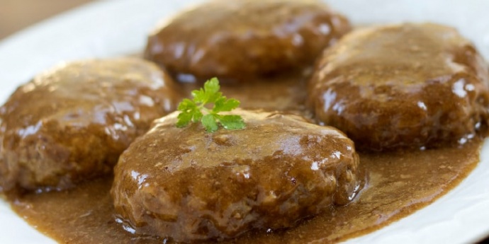 White plate with hamburger patties covered with brown gravy and garnished with a sprig of parsley.