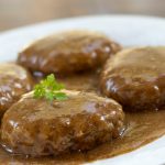 White plate with hamburger patties covered with brown gravy and garnished with a sprig of parsley.