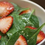 spinach leaves and sliced strawberrys tossed with dressing in a white bowl