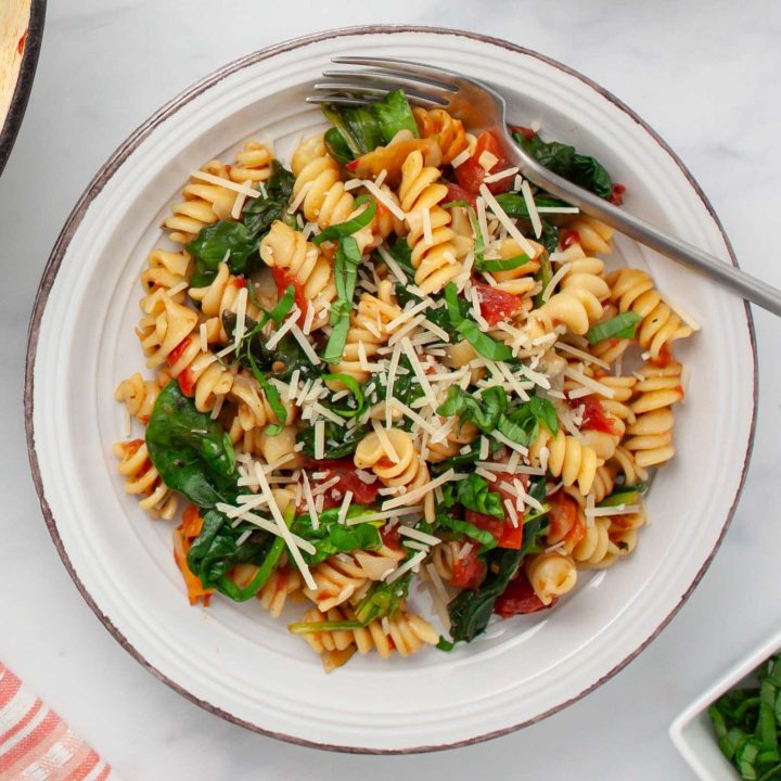 Plate of tomato Spinach Pasta garnished with Parmesan cheese and fresh basil strips.