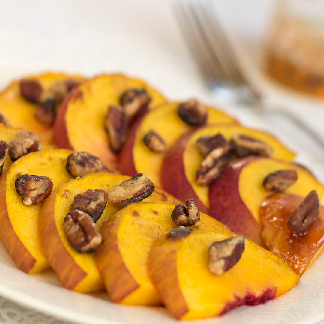 White plate with peach slices topped with chopped pecans. 