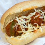 Meatballs, sauce, shredded mozarrella cheese, and strips of bell peppers on a hot dog bun, all on a white plate.