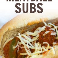 Meatballs, sauce, shredded mozarrella cheese, and strips of bell peppers on a hot dog bun, all on a white plate.
