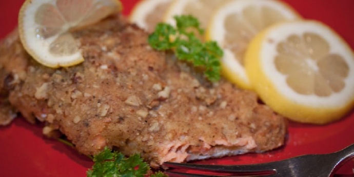 Pecan crusted salmon on a red plate with a fork, garnished with lemon slices and sprigs of parsley.