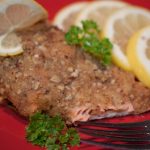 Pecan crusted salmon on a red plate with a fork, garnished with lemon slices and sprigs of parsley.